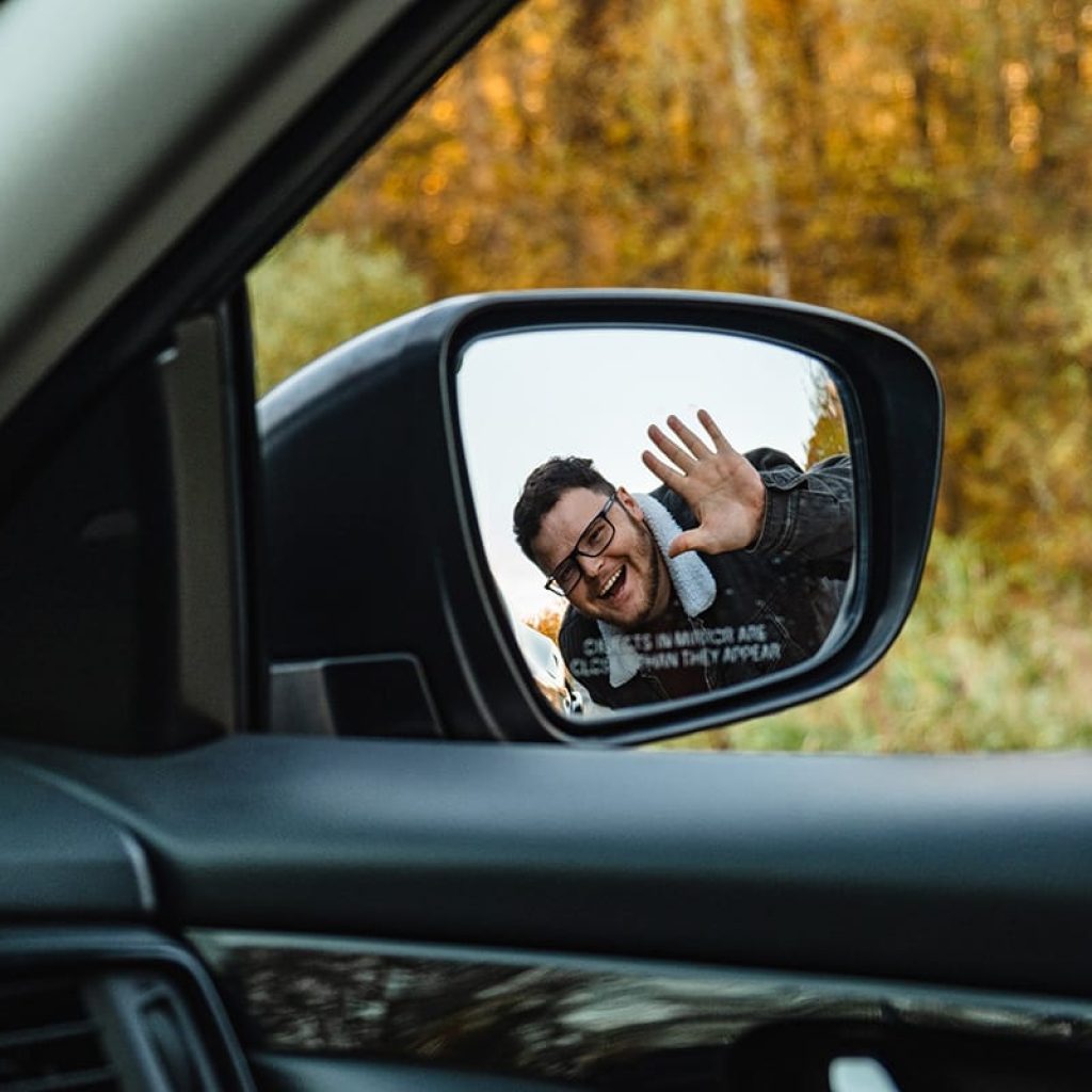 smiling man in the side mirror of the car in the a 2023 11 27 05 25 40 utc x